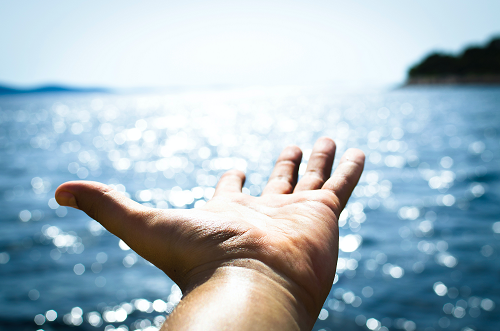 A hand reaching towards a sparkling lake.