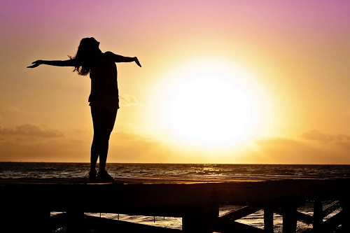 The sillouhette of a woman on a dock at sunset.